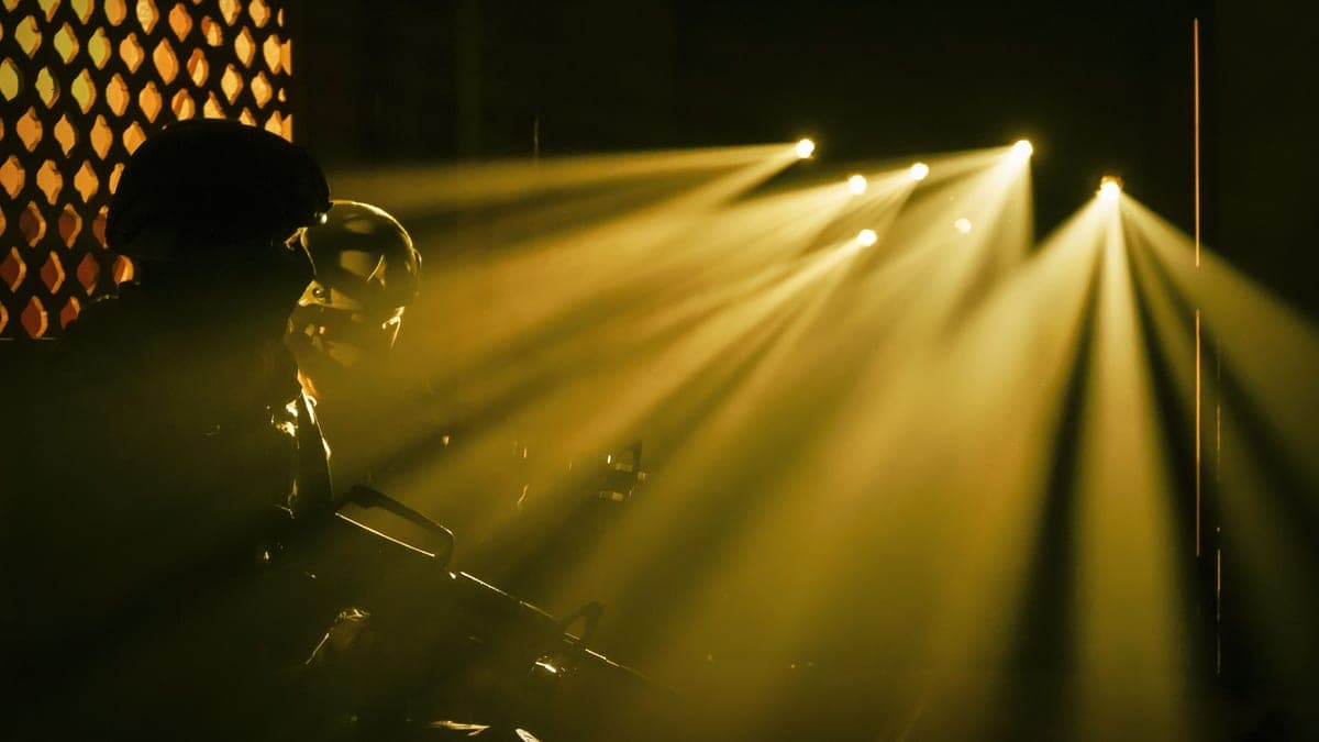 A silhouetted figure holding a rifle under beams of light at night